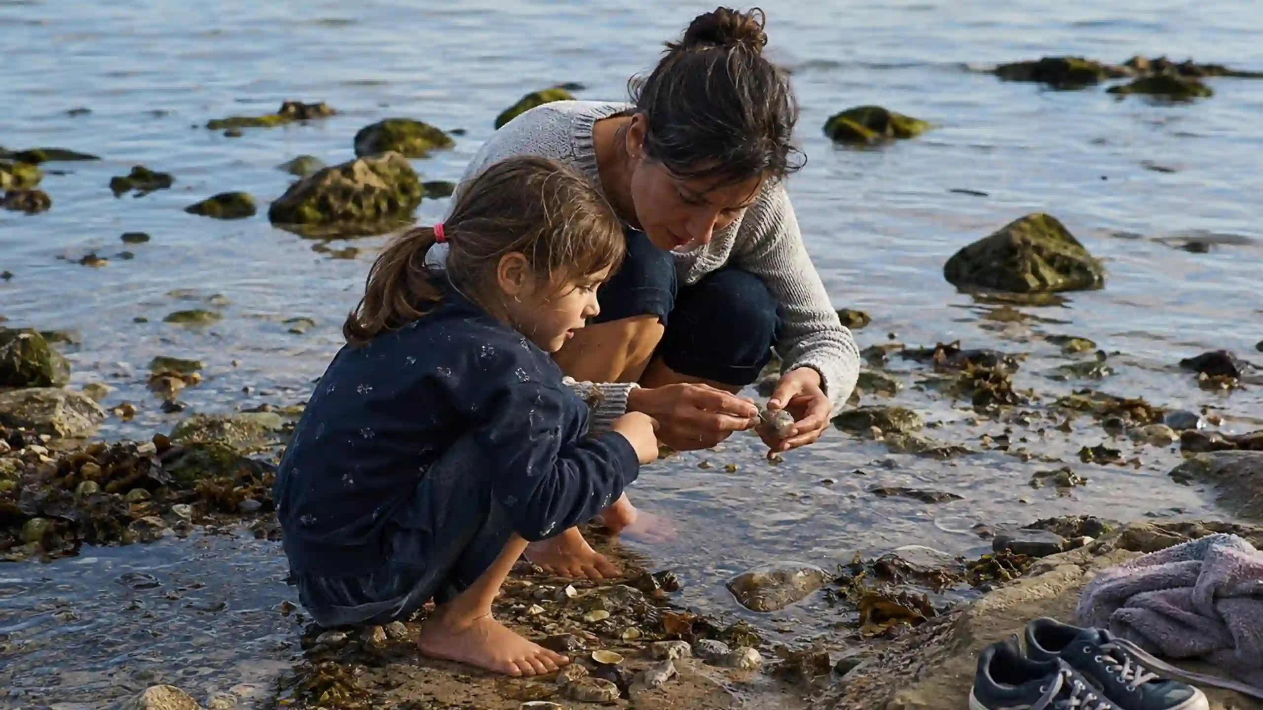 Matka s dieťaťom rozmýšľajú nad Bohom pri morskom pobreží skúmajú v plytkej vode mušle, riasy a malé morské živočíchy